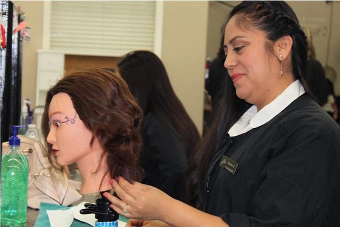 A dedicated cosmetology student practicing an intricate updo on a mannequin head, showing the focused classroom hours needed to master the artistry of hairstyling.