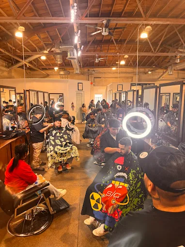 A high-energy training session at the Lawrence & Company Cosmetology school in clovis and hanford, ca student salon, where several barbering students are performing precision haircuts on live clients. The spacious facility features industrial ceilings, professional styling stations with large mirrors, and bright ring lights to ensure detailed work. This hands-on environment is designed to build the technical proficiency and confidence students need to function as future barbering entrepreneurs.